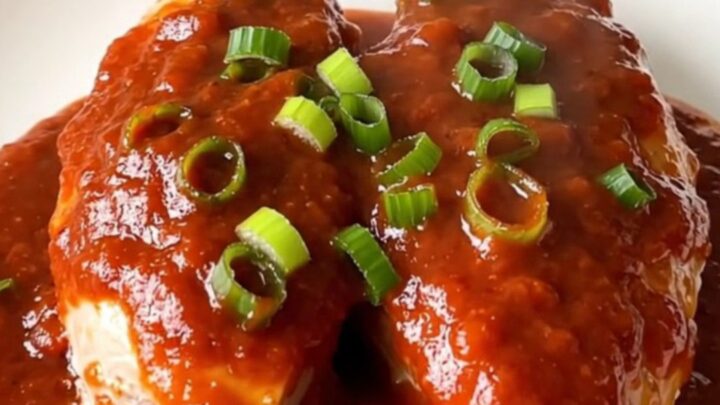 A white oval slow cooker filled with raw turkey tenderloins, green onions, and a vibrant red gochujang sauce.