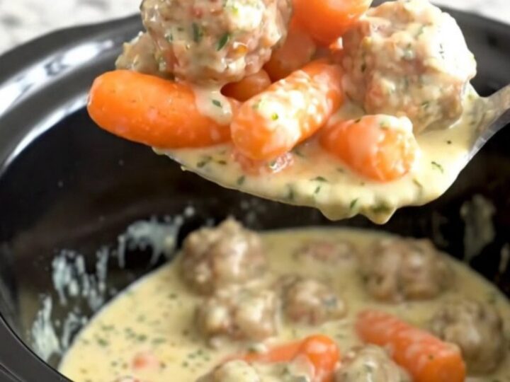 A slow cooker filled with turkey meatballs and baby carrots coated in a creamy herb cheese sauce.