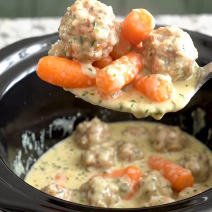 A slow cooker filled with turkey meatballs and baby carrots coated in a creamy herb cheese sauce.