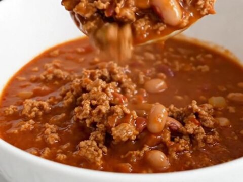 A shallow white bowl filled with hearty ground pork and pinto bean chili, garnished with a spoon.