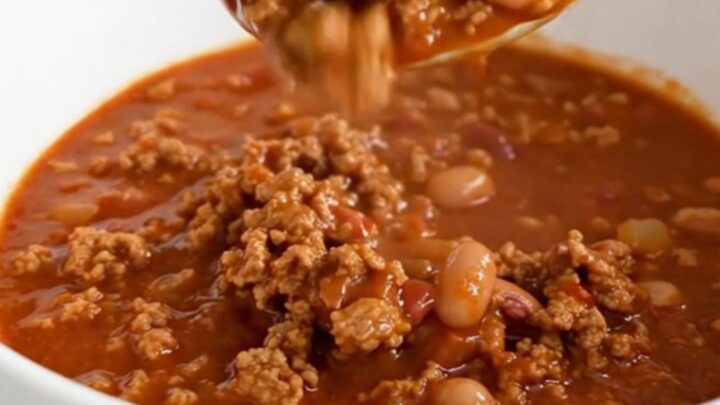 A shallow white bowl filled with hearty ground pork and pinto bean chili, garnished with a spoon.