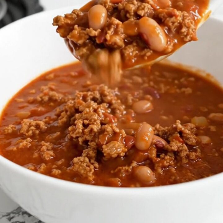 A shallow white bowl filled with hearty ground pork and pinto bean chili, garnished with a spoon.