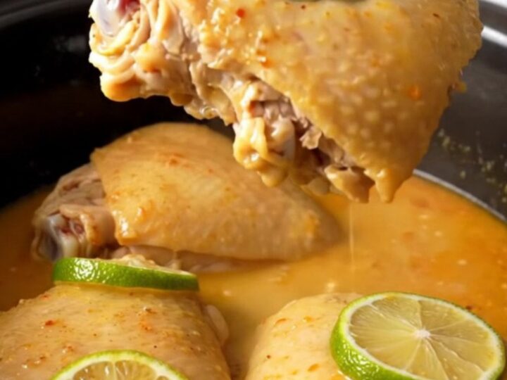 A top-down view of six raw chicken thighs arranged in a white ceramic slow cooker insert, ready to be seasoned.