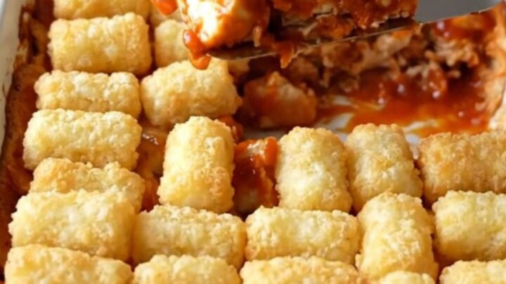 A top-down view of a golden, crispy Nashville hot chicken and potato tot casserole in a white baking dish.