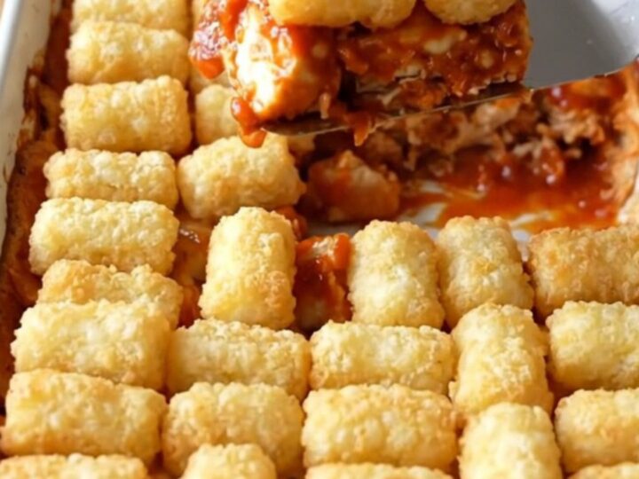 A top-down view of a golden, crispy Nashville hot chicken and potato tot casserole in a white baking dish.