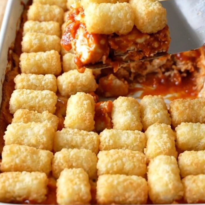 A top-down view of a golden, crispy Nashville hot chicken and potato tot casserole in a white baking dish.