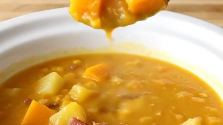 A steaming bowl of creamy orange butternut squash and bacon chowder on a wooden table.