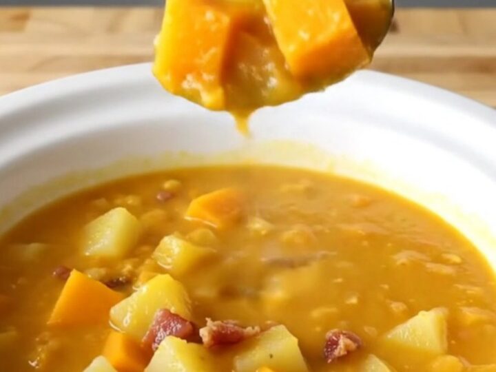 A steaming bowl of creamy orange butternut squash and bacon chowder on a wooden table.