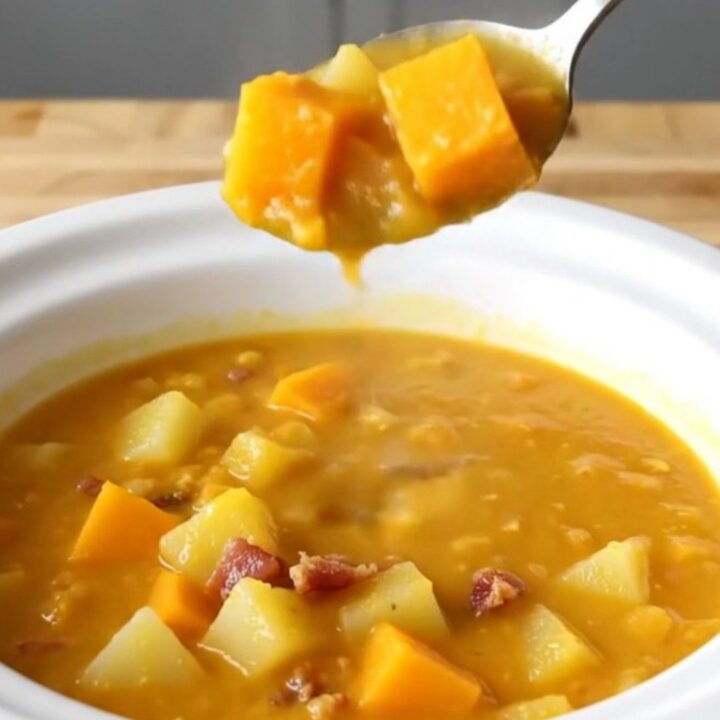 A steaming bowl of creamy orange butternut squash and bacon chowder on a wooden table.