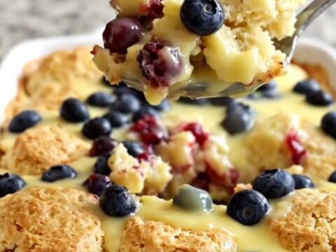A golden, baked lemon blueberry biscuit casserole in a white ceramic dish, steaming slightly.