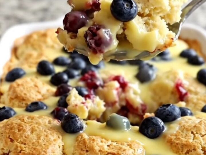 A golden, baked lemon blueberry biscuit casserole in a white ceramic dish, steaming slightly.