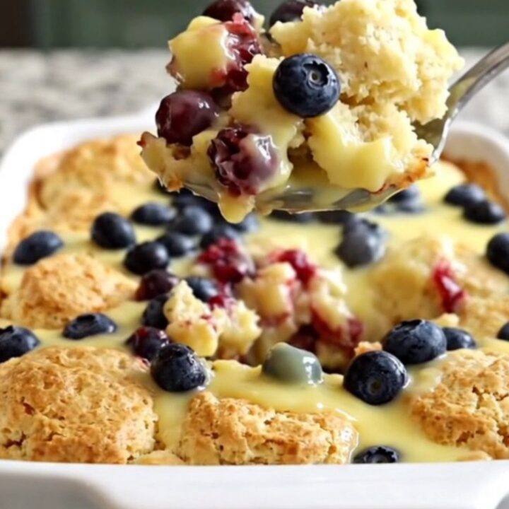 A golden, baked lemon blueberry biscuit casserole in a white ceramic dish, steaming slightly.