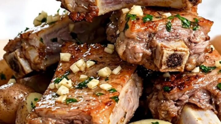 A close-up of slow-cooked pork spareribs and baby potatoes coated in a glistening garlic butter sauce.