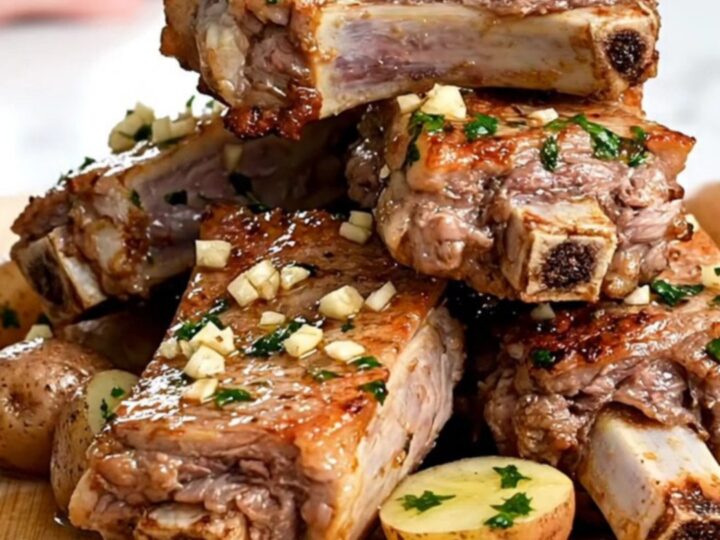 A close-up of slow-cooked pork spareribs and baby potatoes coated in a glistening garlic butter sauce.