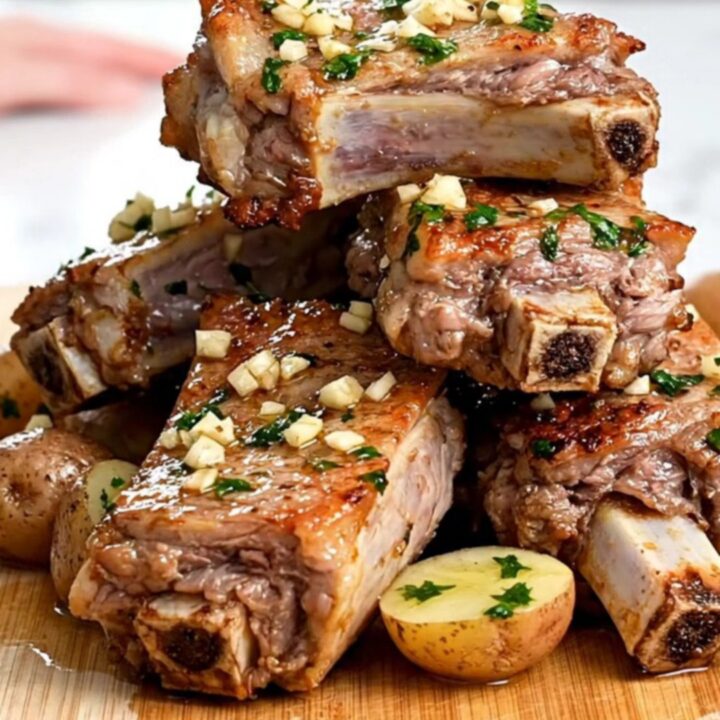 A close-up of slow-cooked pork spareribs and baby potatoes coated in a glistening garlic butter sauce.
