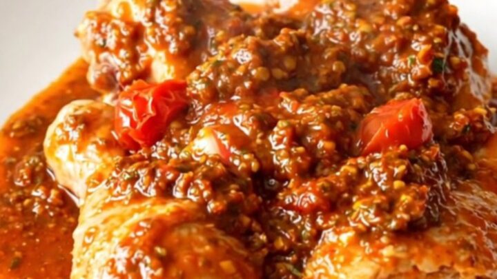 A close-up of tender, slow-cooked chicken drumsticks coated in a vibrant red sun-dried tomato pesto sauce on a white plate.