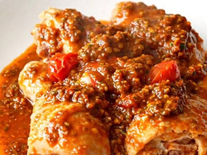 A close-up of tender, slow-cooked chicken drumsticks coated in a vibrant red sun-dried tomato pesto sauce on a white plate.