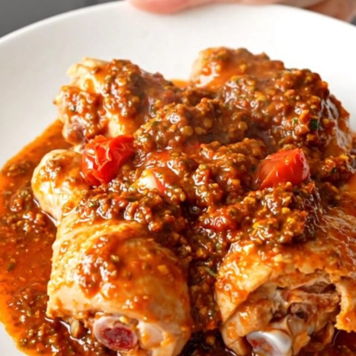 A close-up of tender, slow-cooked chicken drumsticks coated in a vibrant red sun-dried tomato pesto sauce on a white plate.