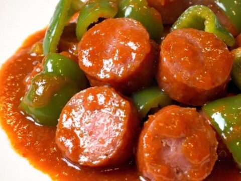 A close-up of honey sriracha kielbasa coins and green peppers in a shiny, red sauce in a slow cooker.