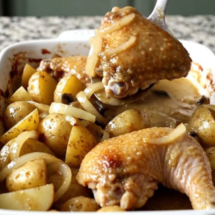 A large rectangular ceramic dish filled with golden baked chicken thighs and potatoes covered in creamy mushroom gravy.