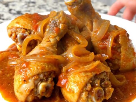 A top-down view of raw chicken drumsticks arranged in a ring in a black slow cooker insert.