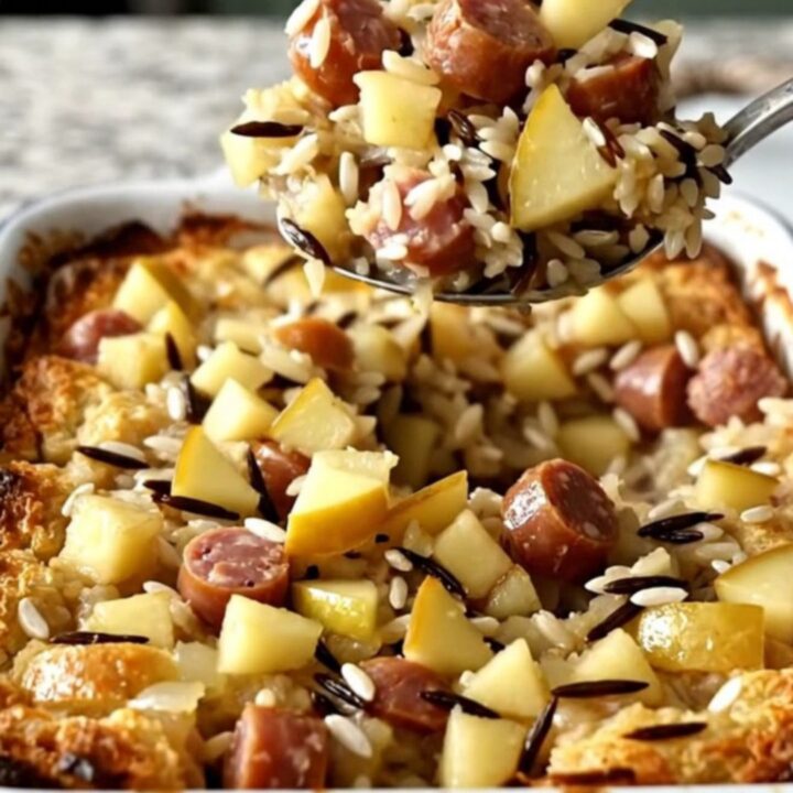 A large white rectangular baking dish filled with a golden, savory wild rice, sausage, and apple bake.