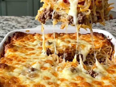 A golden, bubbling bacon cheeseburger hash brown bake in a rectangular ceramic dish on a light granite counter.