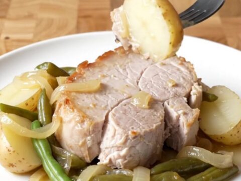 A plate of tender slow-cooked pork loin with soft baby potatoes and green beans, lightly coated in a buttery onion sauce.