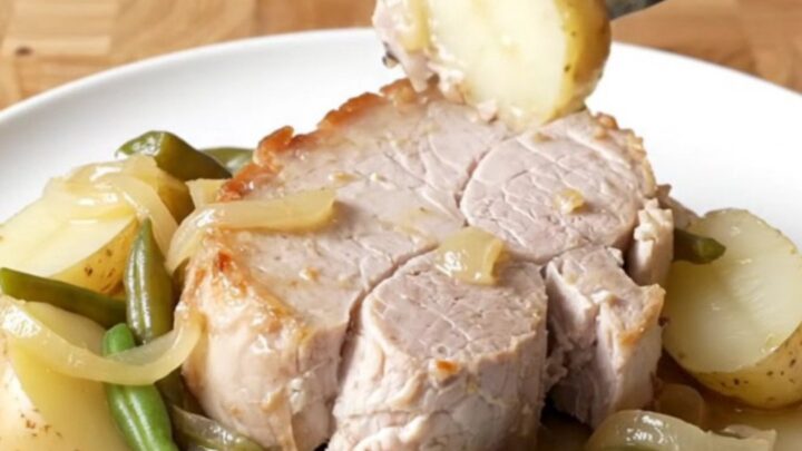 A plate of tender slow-cooked pork loin with soft baby potatoes and green beans, lightly coated in a buttery onion sauce.