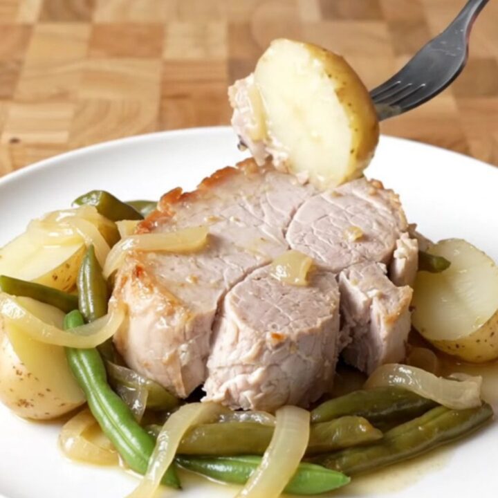 A plate of tender slow-cooked pork loin with soft baby potatoes and green beans, lightly coated in a buttery onion sauce.