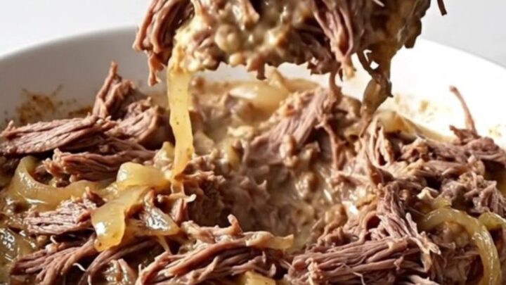 A shallow white bowl filled with creamy shredded beef dip, showing tender meat fibers and melted cream cheese on a marble