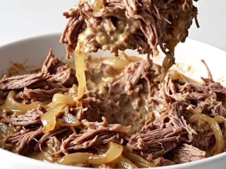 A shallow white bowl filled with creamy shredded beef dip, showing tender meat fibers and melted cream cheese on a marble