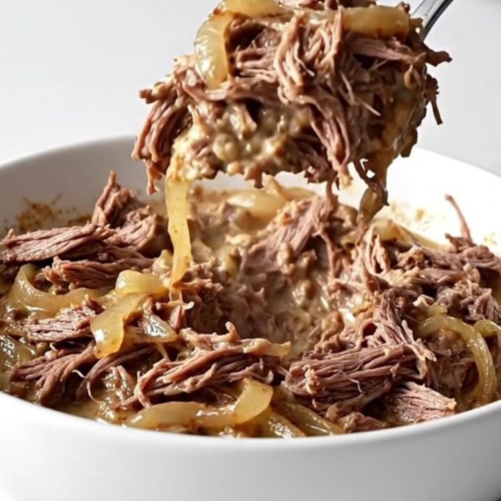 A shallow white bowl filled with creamy shredded beef dip, showing tender meat fibers and melted cream cheese on a marble