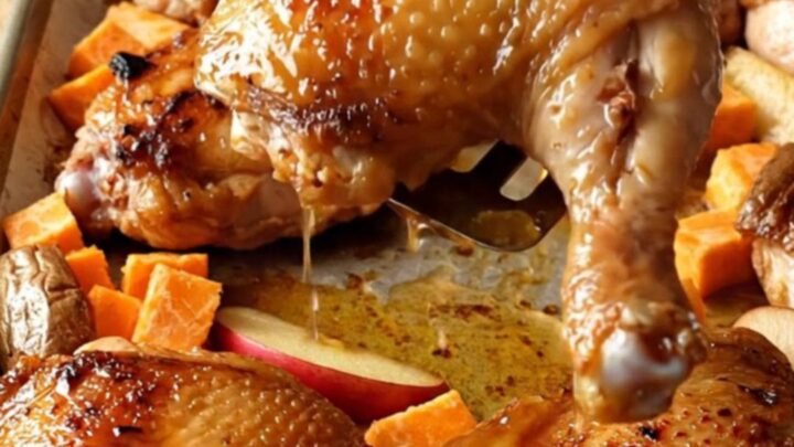 A sheet pan filled with golden-brown roasted chicken thighs, orange sweet potato cubes, and red apple wedges.