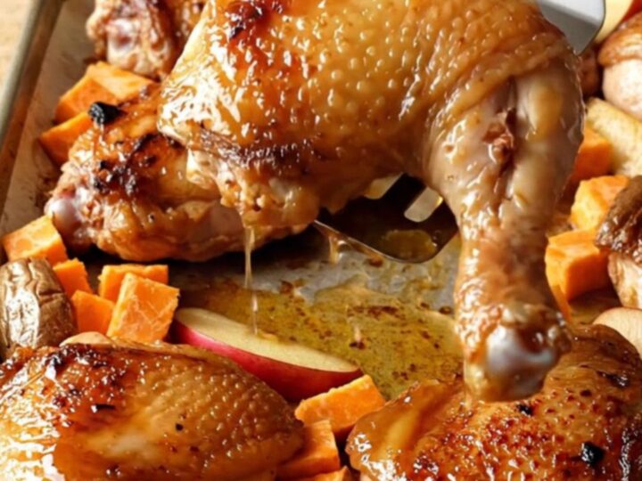 A sheet pan filled with golden-brown roasted chicken thighs, orange sweet potato cubes, and red apple wedges.