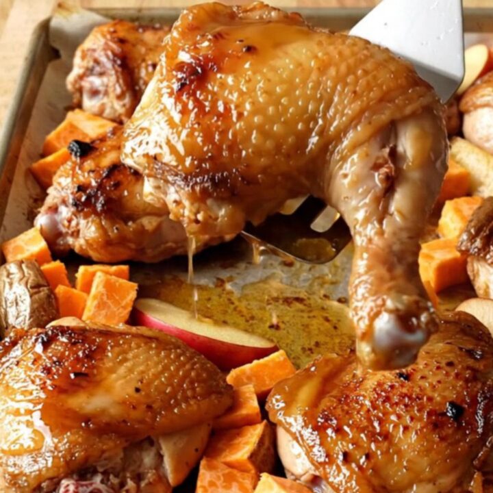 A sheet pan filled with golden-brown roasted chicken thighs, orange sweet potato cubes, and red apple wedges.