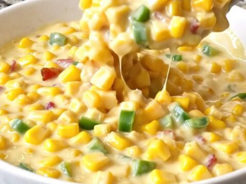 A top-down view of creamy jalapeño popper corn in a black slow cooker insert, showing yellow corn, melted cheese
