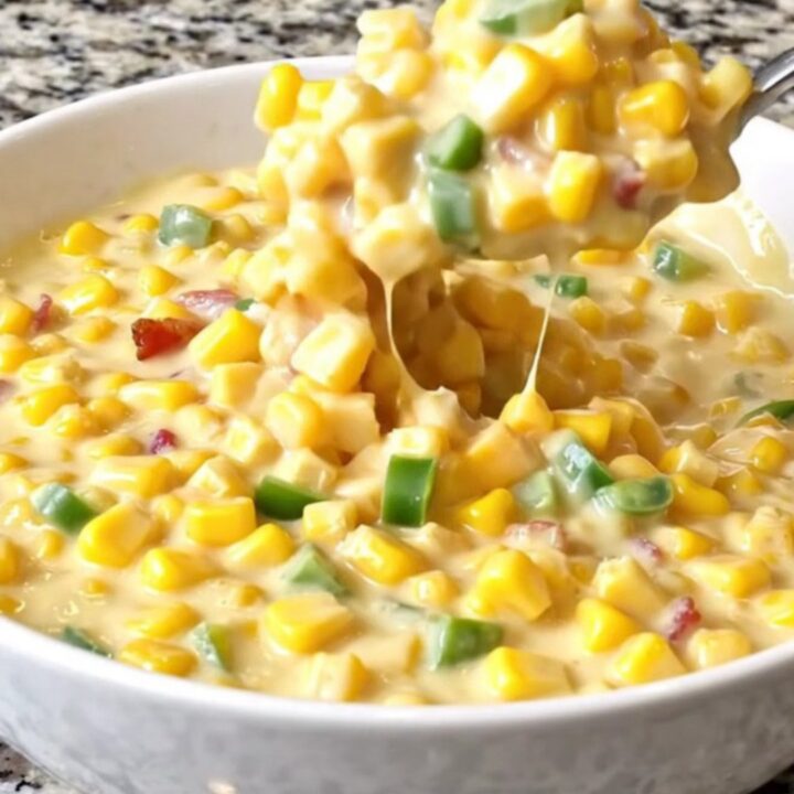 A top-down view of creamy jalapeño popper corn in a black slow cooker insert, showing yellow corn, melted cheese