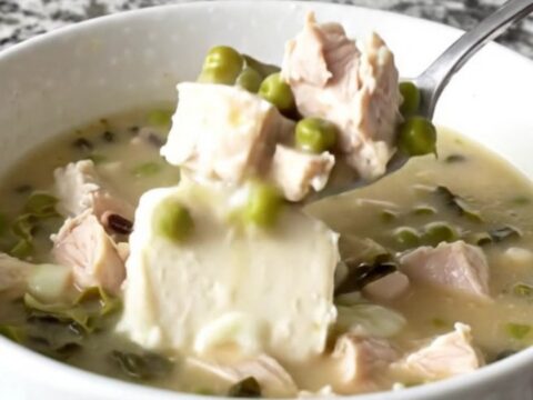 A close-up of creamy Cajun chicken soup in a white bowl, showing tender chicken, black-eyed peas, and collard greens.