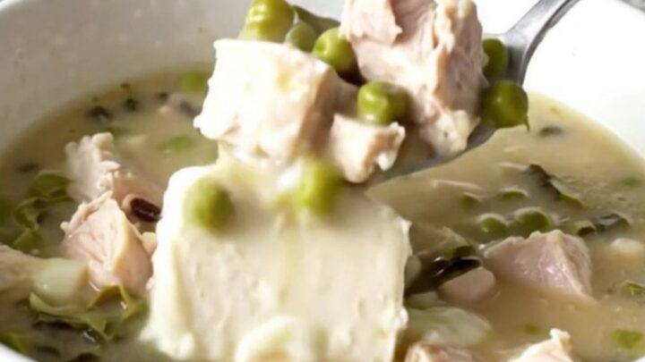 A close-up of creamy Cajun chicken soup in a white bowl, showing tender chicken, black-eyed peas, and collard greens.