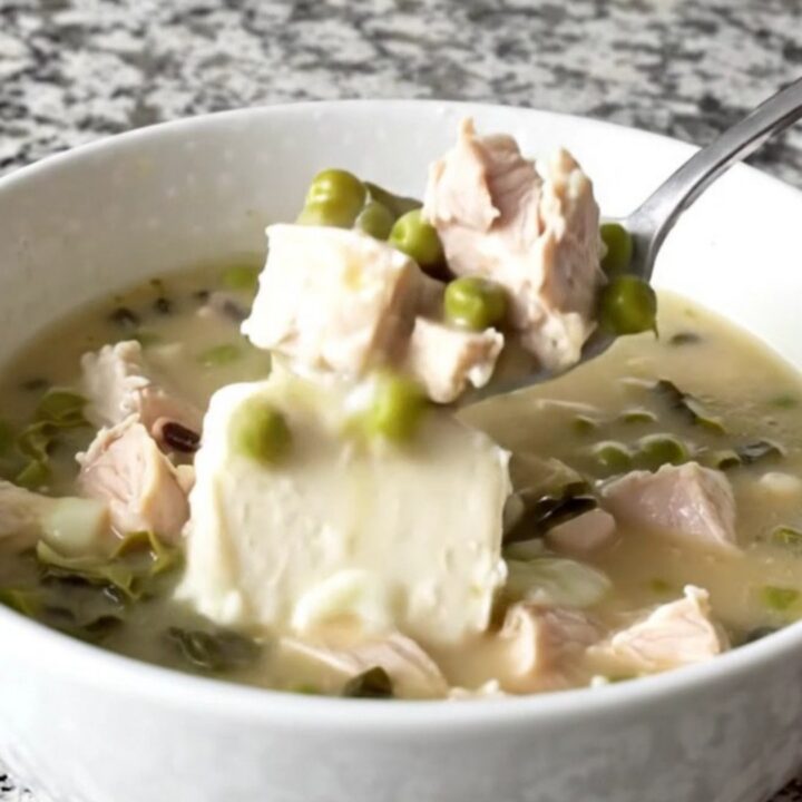 A close-up of creamy Cajun chicken soup in a white bowl, showing tender chicken, black-eyed peas, and collard greens.