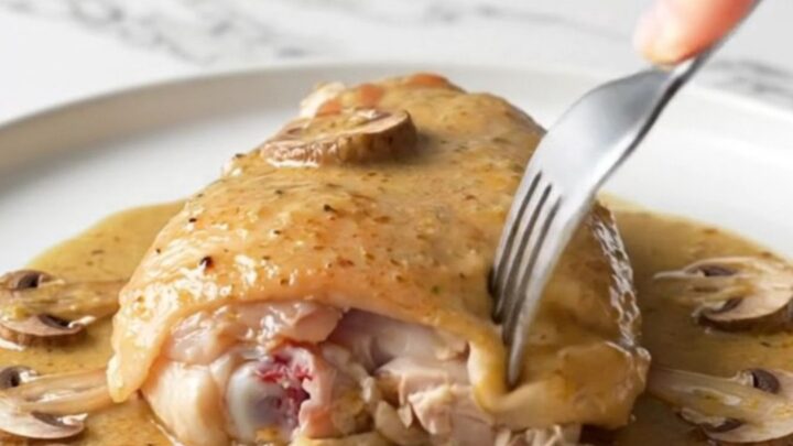 A close-up of tender chicken thighs in a creamy mushroom Marsala sauce served on a white plate.