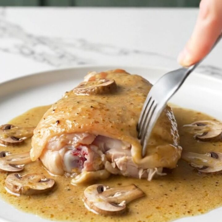 A close-up of tender chicken thighs in a creamy mushroom Marsala sauce served on a white plate.
