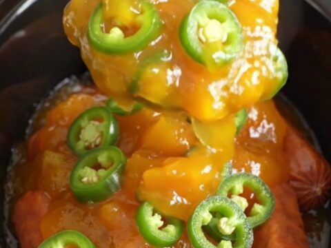 A close-up of slow cooker cocktail sausages coated in a glossy, golden-orange peach and jalapeno glaze.