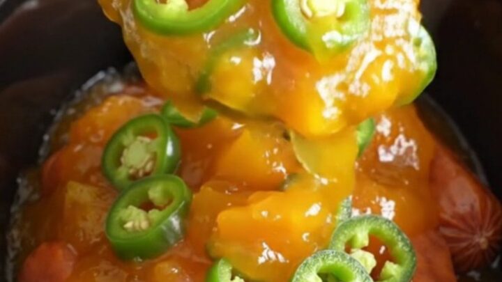 A close-up of slow cooker cocktail sausages coated in a glossy, golden-orange peach and jalapeno glaze.