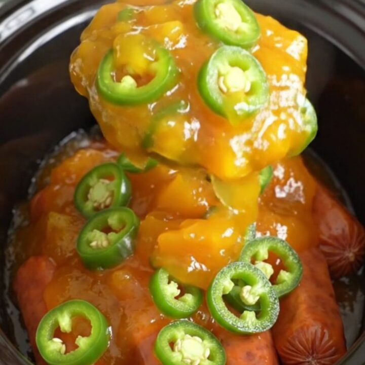A close-up of slow cooker cocktail sausages coated in a glossy, golden-orange peach and jalapeno glaze.