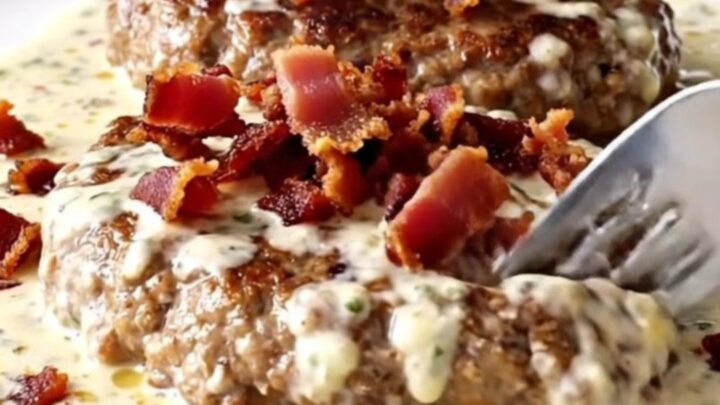 A plate featuring a cooked turkey burger steak covered in a rich, creamy ranch sauce and topped with crispy bacon.