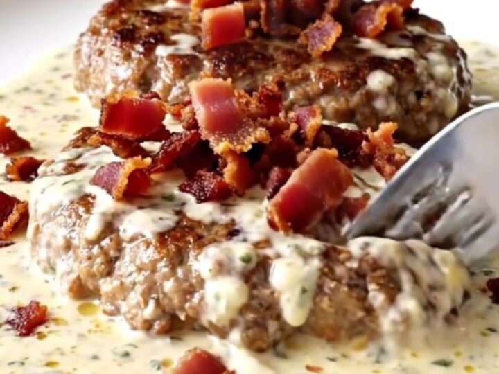 A plate featuring a cooked turkey burger steak covered in a rich, creamy ranch sauce and topped with crispy bacon.
