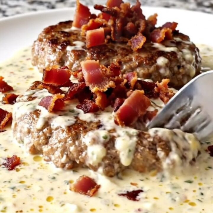 A plate featuring a cooked turkey burger steak covered in a rich, creamy ranch sauce and topped with crispy bacon.