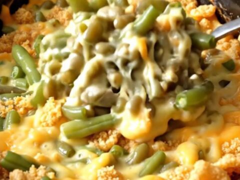 A close-up view of the creamy green bean bake inside a black slow cooker insert, showing melted cheese and green beans.